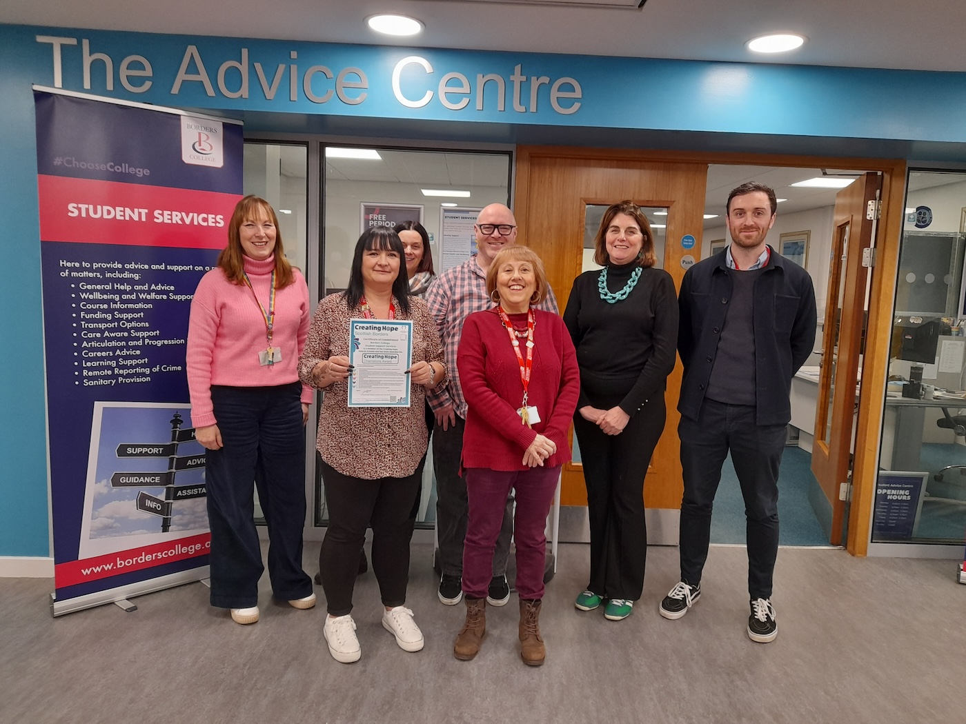 Group of people standing outside an office setting with one person holding a Creating Hope Champions Award certificate 
