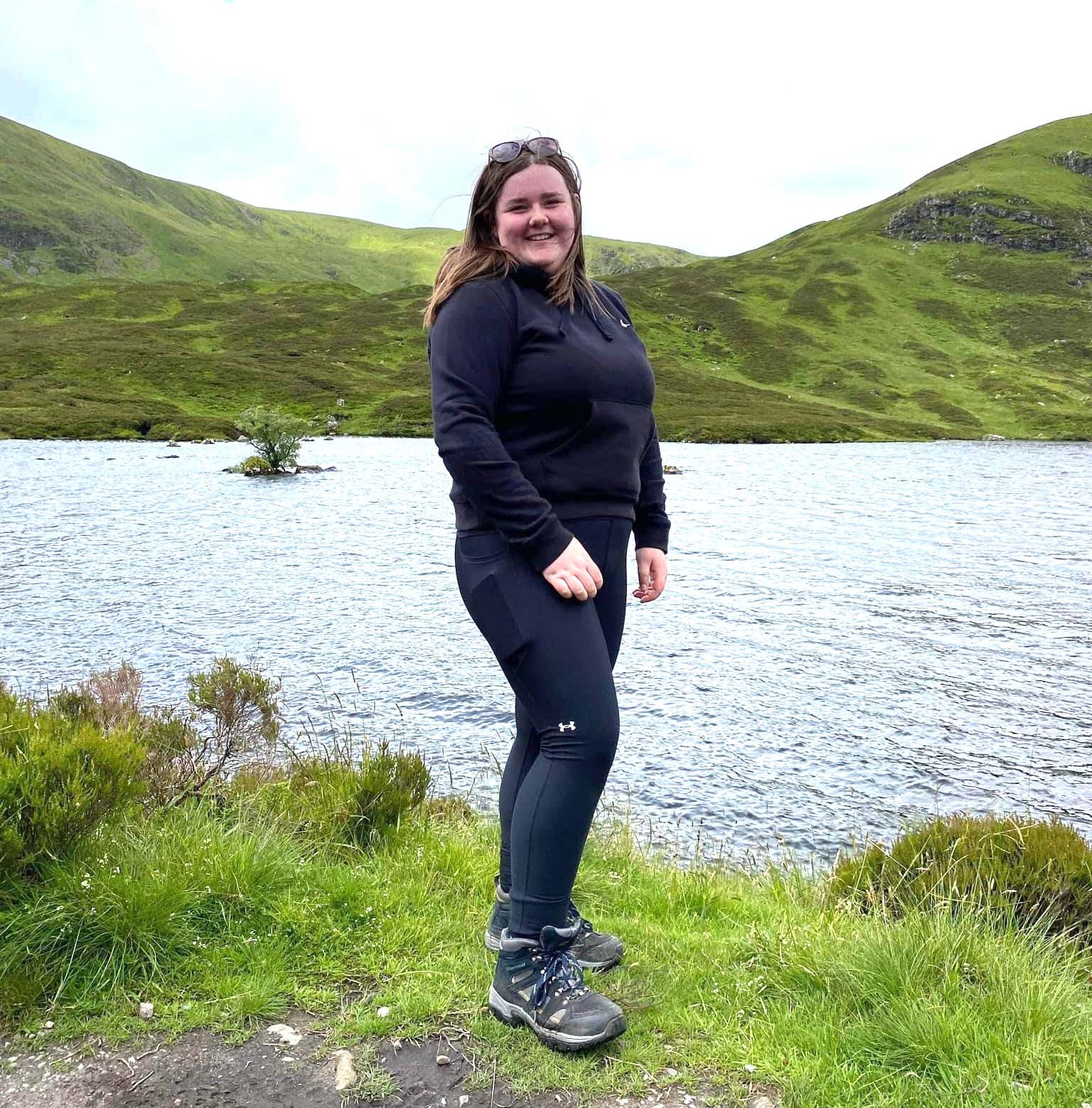 Photo showing a woman standing on a banking next to a body of water. 