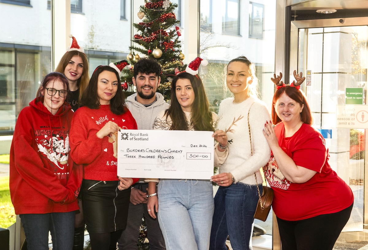 Group of students holding a cheque within a xmas theme setting.