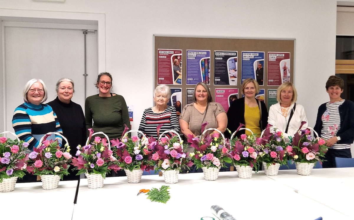 Group of students standing behind a table with flower baskets sitting in front of them.