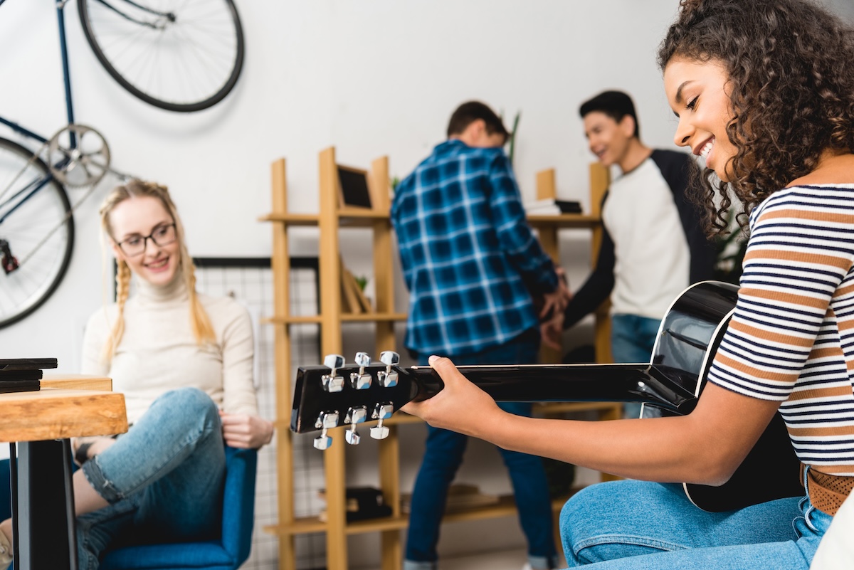 Photograph of a person playing the guitar with people in the background spectating.