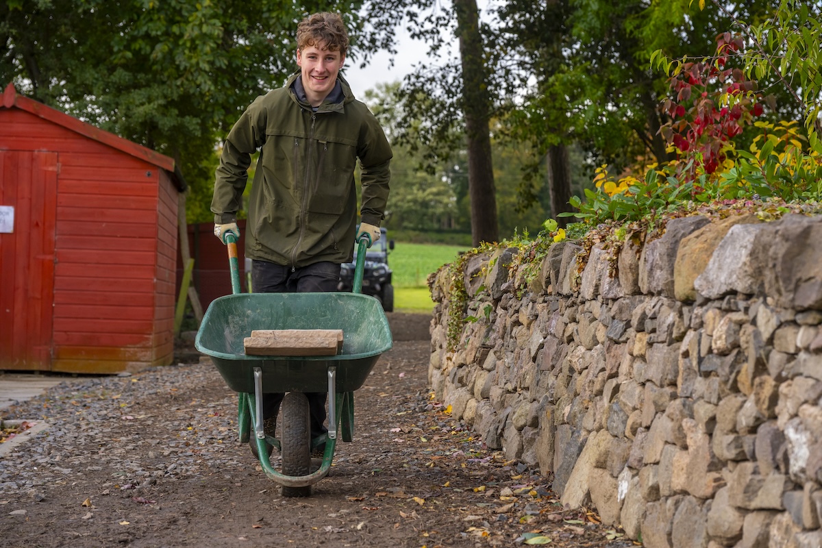 Landscaping student pictured in an outside setting pushing a wheelbarrow