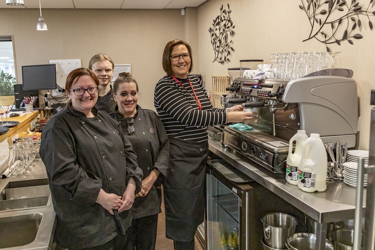 staff and students standing in a restaurant setting using a coffee machine
