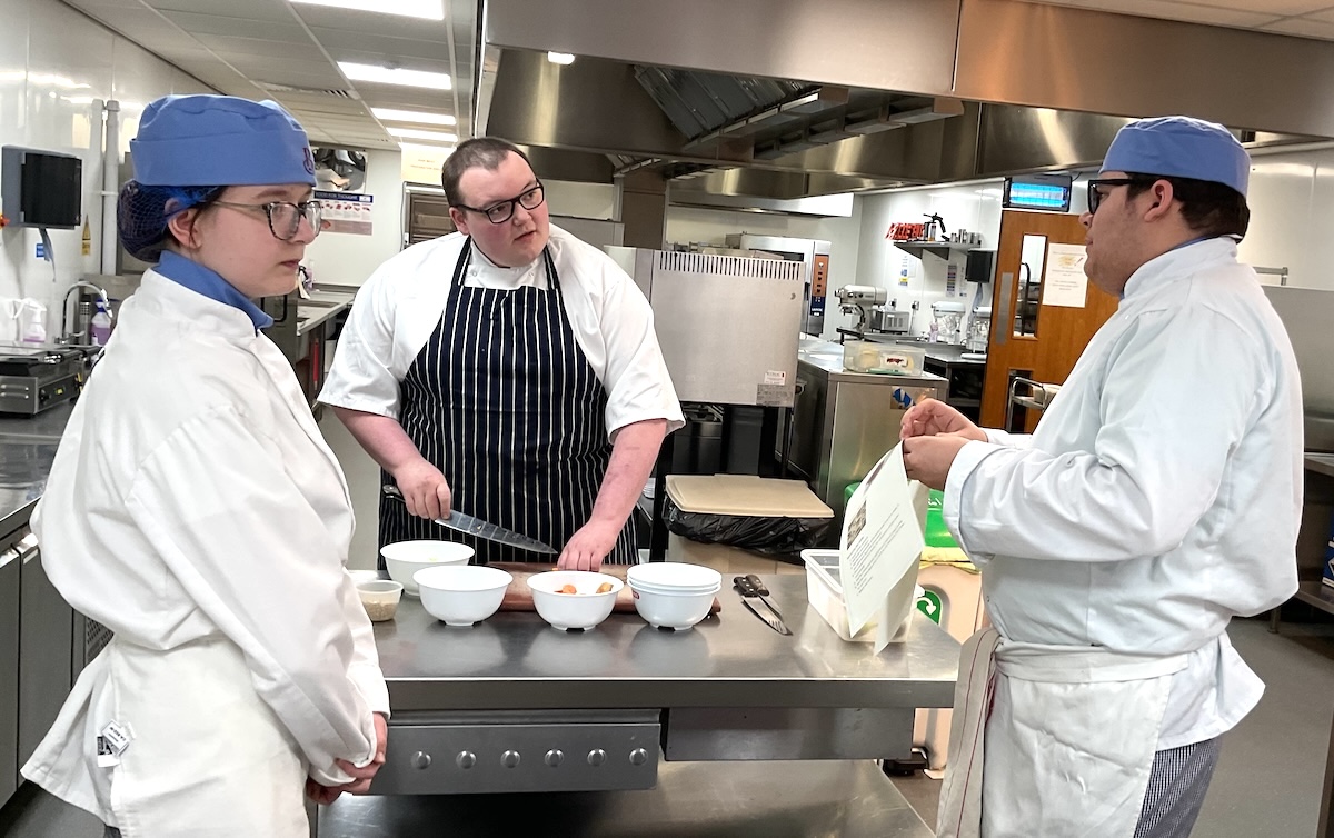 Catering students and guest chef Angus Levell standing having a discussion in a kitchen setting