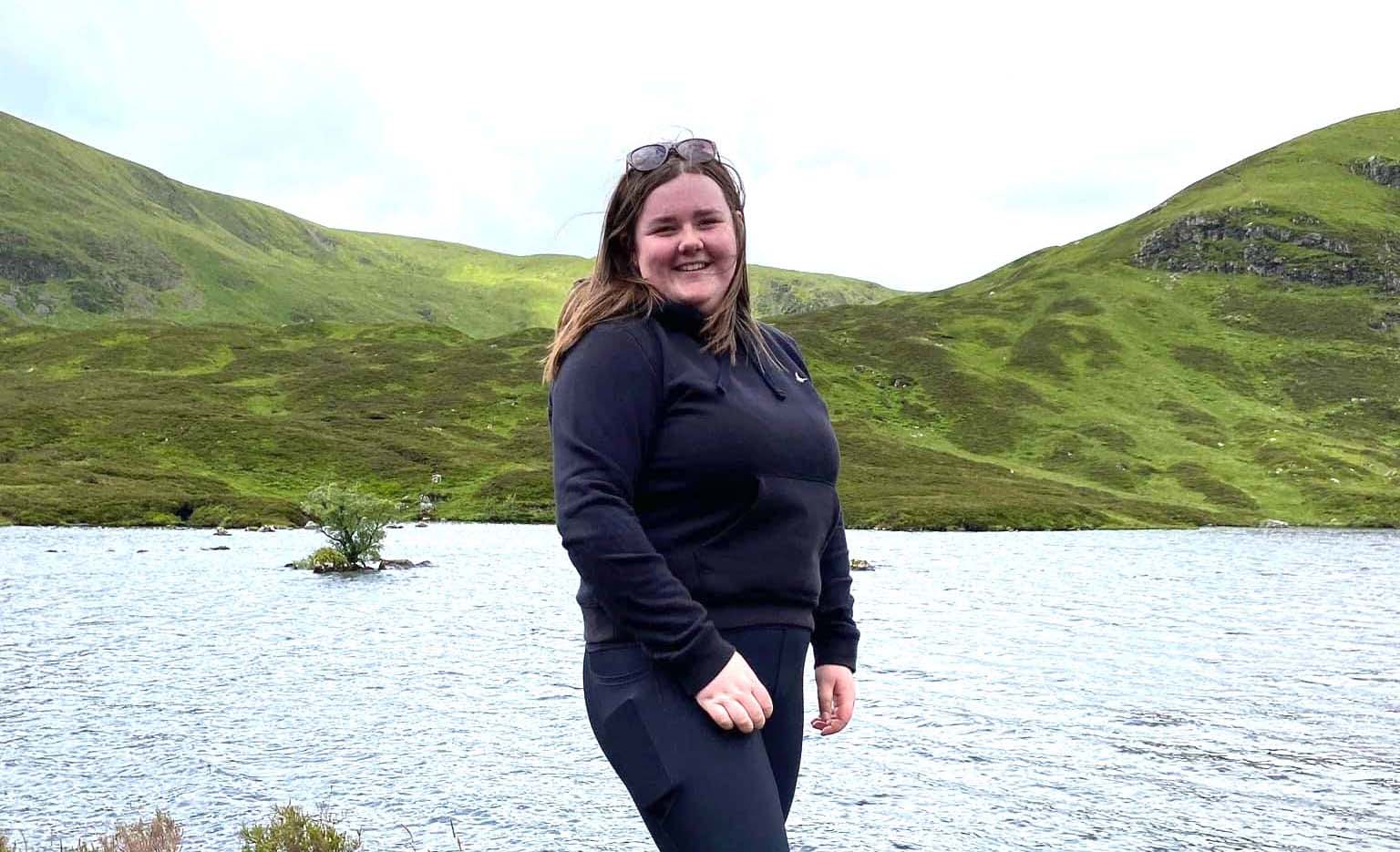 Photo of Sophie Redpath standing next to a body of water with hills in the background