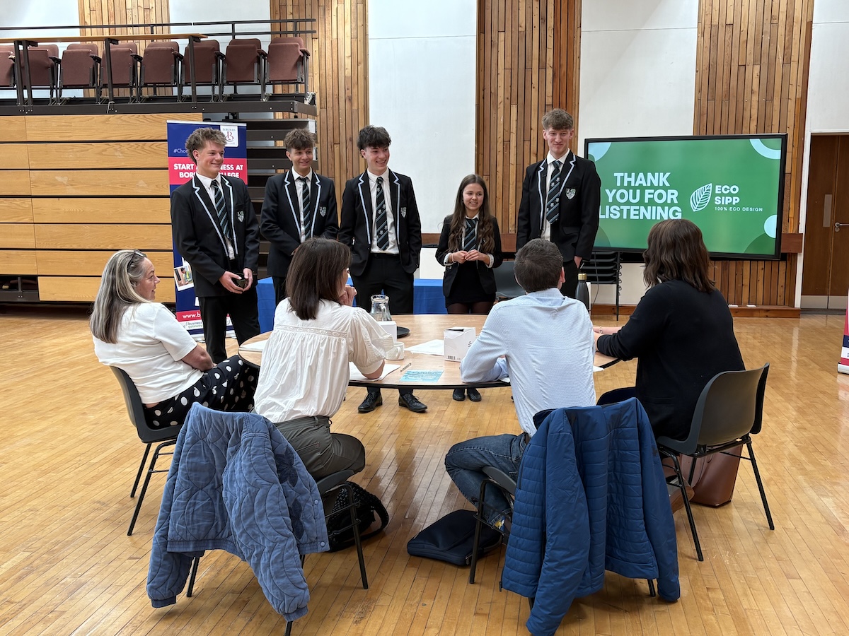 Group of students standing having a discussion with a panel of judges in an educational setting