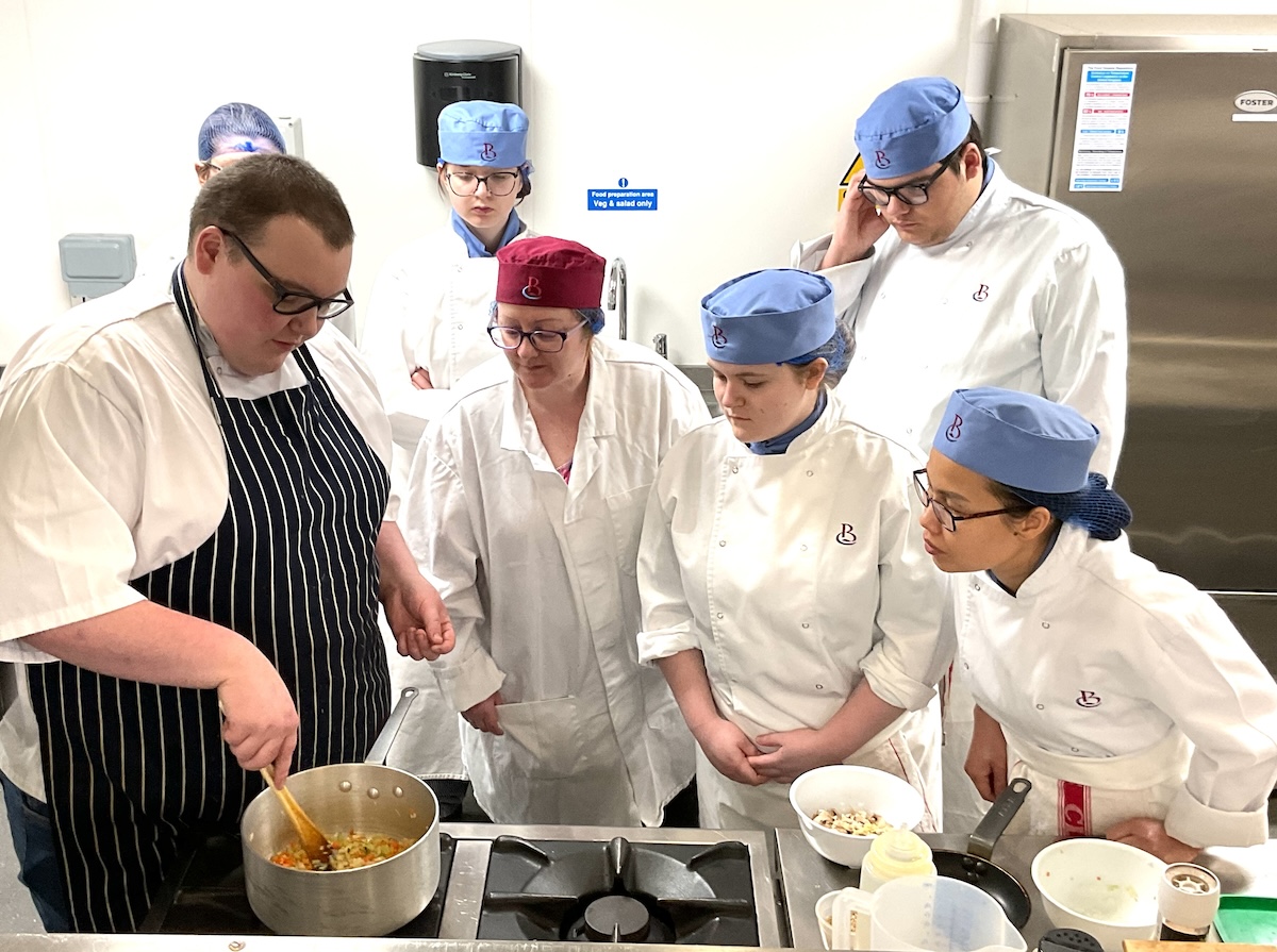 A group of catering students observing a culinary demonstration in a kitchen setting