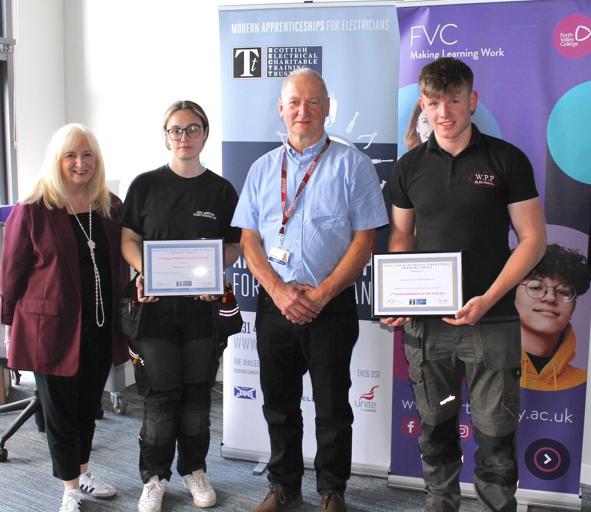 Photograph of 2 students standing holding competition certificates alongside 2 other people