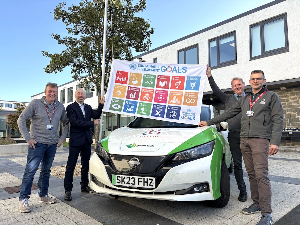 Four people standing next to a car holding the SDG flag
